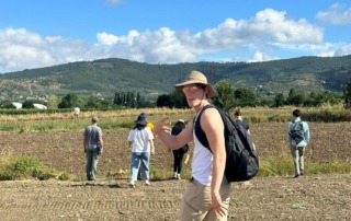 Archaeology students participating in a field survey near Cortona, walking through an open field with mountains in the background.