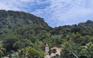 A picturesque view of a church surrounded by dense forest and mountains in Pohnpei.