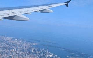 View from an airplane window showing the city skyline and coastline below, symbolizing the journey of returning home after field school abroad