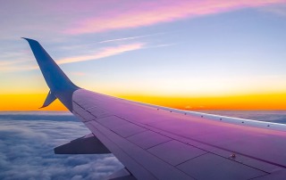 View from an airplane window of the wing and vibrant sunset sky above the clouds, symbolizing the experience of returning home from an adventure