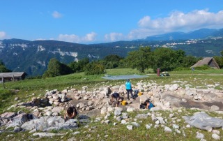 Archaeology students excavating an ancient site in the Bostel di Rotzo region of Vicenza, Italy, surrounded by scenic mountain views.