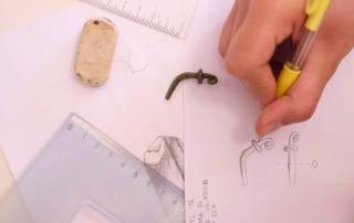 Close-up of a student sketching an artifact with ruler and drawing tools, documenting finds at the Bostel di Rotzo field school in Italy