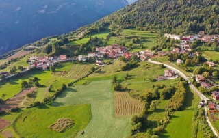 Aerial view of the Bostel di Rotzo village and archaeological site in Vicenza, Italy, with green fields and mountain landscape.