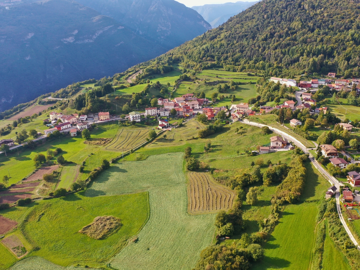 Aerial view of the Bostel di Rotzo village and archaeological site in Vicenza, Italy, with green fields and mountain landscape.