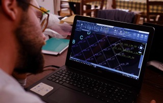 Archaeology student working on digital mapping of excavation grids on a laptop at Bostel di Rotzo, Italy.