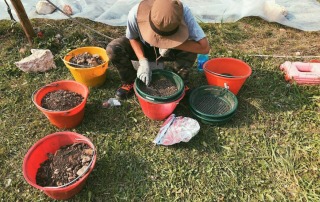 Archaeology student sorting artifacts using different colored buckets and screens at Bostel di Rotzo, Italy.
