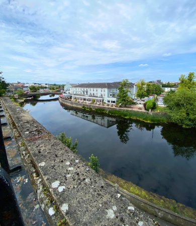 Calm river reflecting buildings and greenery in Kilkenny, Ireland, offering a peaceful view of the town on a clear day