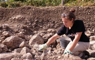 Close-up of a student using a trowel to excavate ancient artifacts at a field school in Vicenza, Italy, focusing on hands-on archaeological training.