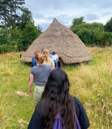 Group of students walking towards a traditional thatched hut built at University College Dublin, participating in an archaeology field school in Ireland