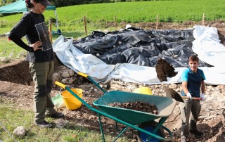 Field school students using a wheelbarrow to remove soil at an excavation site in Vicenza, Italy, as part of practical archaeological training.
