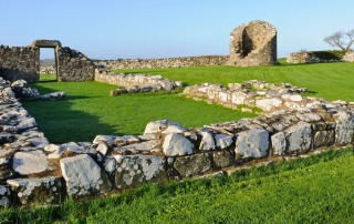 Stone ruins of a monastic structure in a green field under a clear blue sky in Ireland, representing an archaeology field school setting