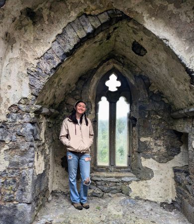 A student stands in a Gothic arch window at a historical site in Ireland, participating in an archaeology field school