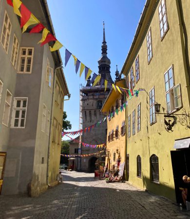 A colorful alleyway leading to the Clock Tower in Sighisoara, Romania, lined with historic buildings and festive decorations.