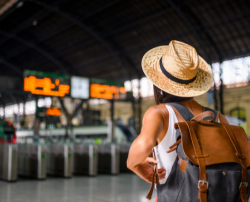 A traveler with a hat and backpack looking at train schedules in a station, emphasizing travel readiness.