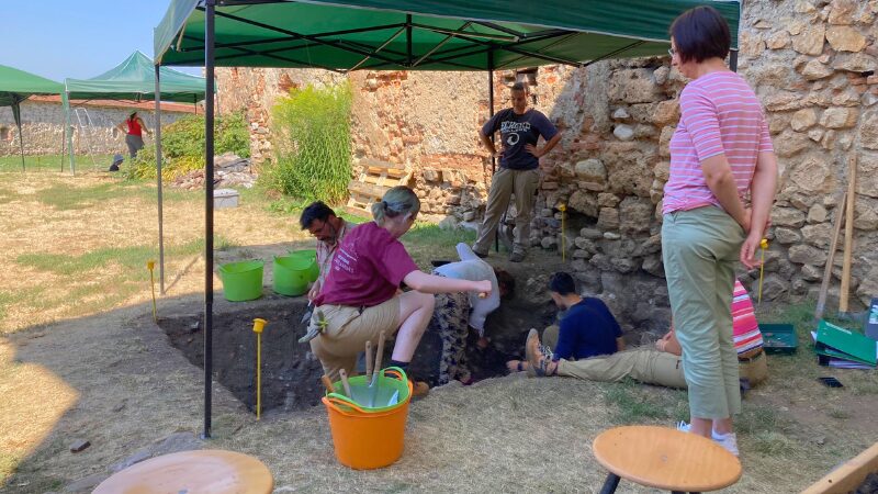 Excavation site at Romania: Sanpetru field school Group of archaeology students working under shade canopies at the Sanpetru excavation site in Romania, carefully unearthing and documenting finds.