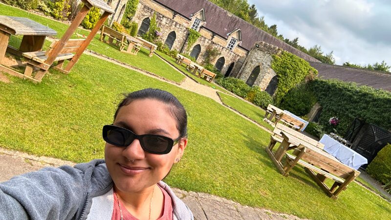 Day trip to Kinnitty Castle, Ireland A student poses for a selfie in the garden courtyard of Kinnitty Castle in Ireland, surrounded by historic stone buildings and vibrant greenery.