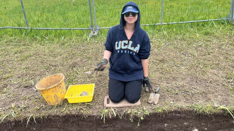 archaeology-student-Meredith-excavating-green-fort-ireland Archaeology student kneeling with tools and artifacts during excavation at the Green Fort site in Sligo, Ireland.