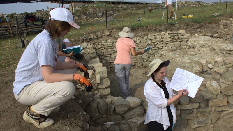 Archaeology field school students documenting and sketching excavation trench features, practicing observation and recording techniques.
